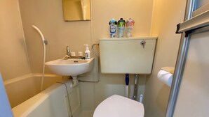 A small bathroom with a white sink, toilet, and shower. There are toiletries on the sink and a mirror above it.