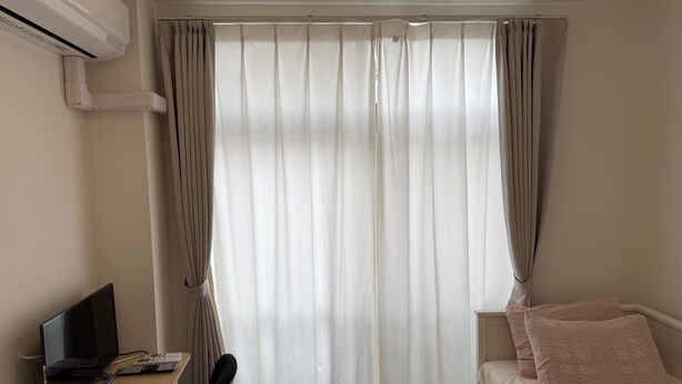 Quarto com uma cama, uma escrivaninha com computador e janela com cortinas.