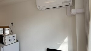 Pared branca com ar condicionado fixado e micro-ondas sobre um armário branco.