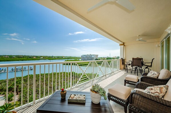 A balcony with wicker furniture, a table with decorative items, and a view of a river and distant buildings. - 🐬Stunning Intracoastal Views, Great Location-Dolphin Key 504🐬 (Indian Shores)