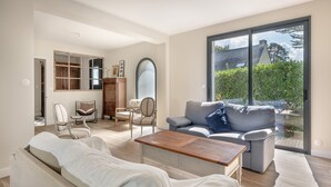 Un salon spacieux avec une grande fenêtre, un canapé, une table basse et un meuble en bois.