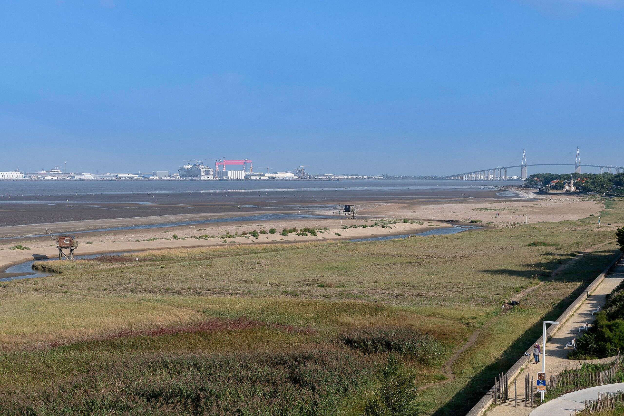 Kustlandschap met een brug, strand en uitkijkplatform.
