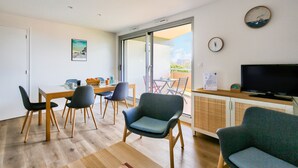 A modern living room with a dining area, a television, and a sliding glass door leading to an outdoor patio. - 130m from the beach, nice flat for 4 (Pléneuf-Val-André)