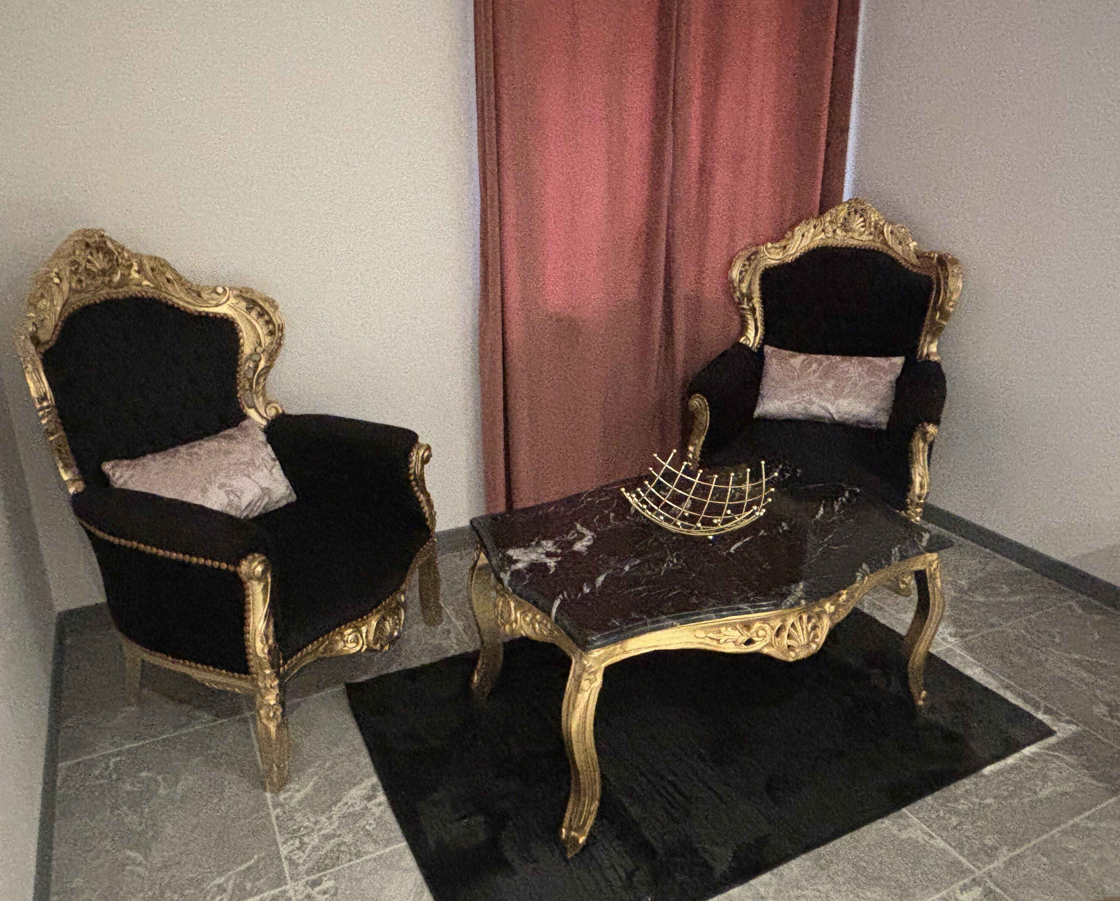 Twee sierlijke stoelen met gouden accenten, een marmeren tafel en een rode gordijn op de achtergrond.