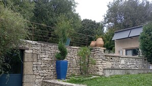 A stone wall with a blue planter and a small tree, a stone staircase, and a house with a sloped roof.