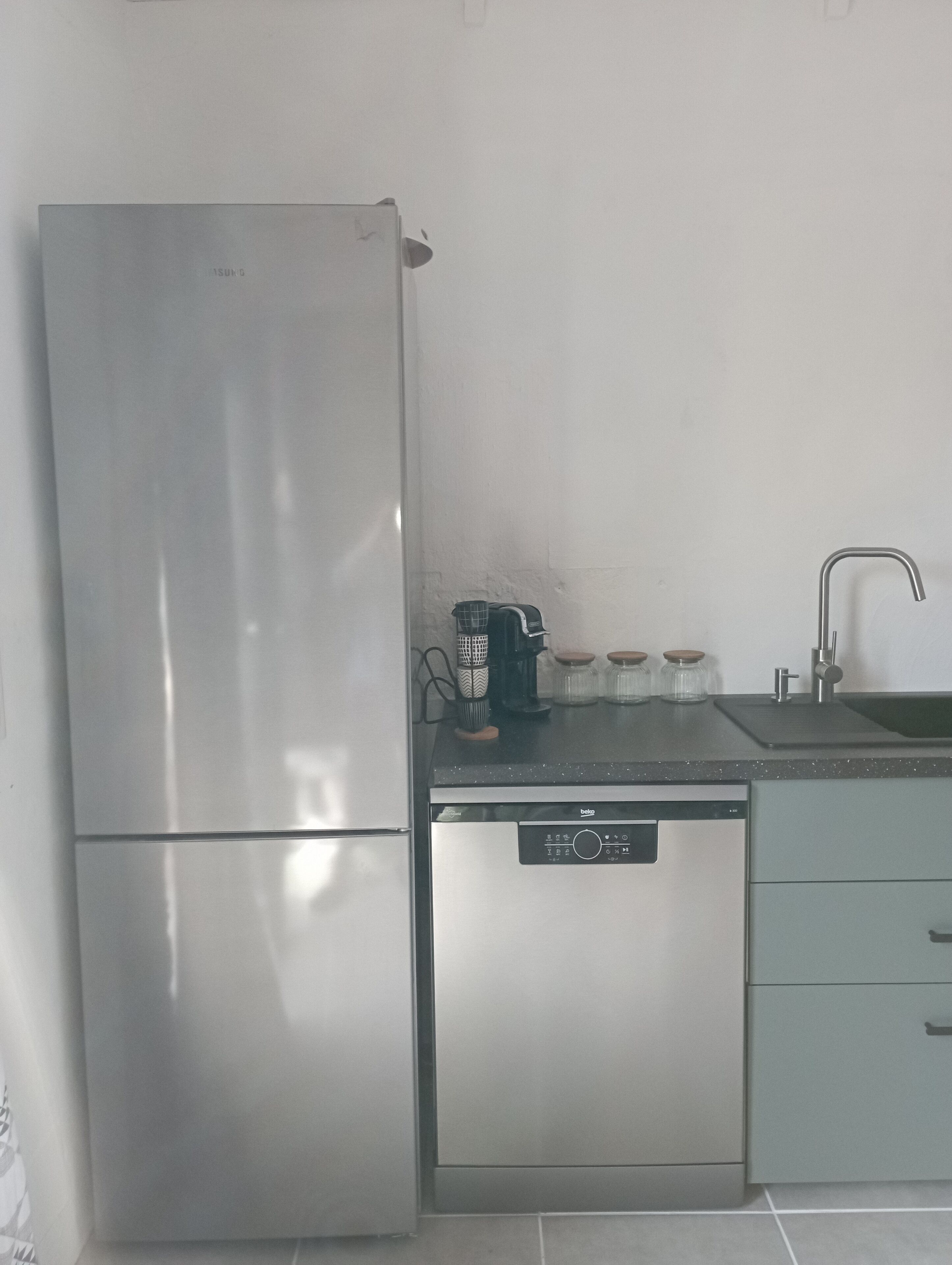 Et køkken med et rustfrit stål køleskab, opvaskemaskine, kaffemaskine og en vask.