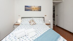 A neatly made bed with a patterned bedspread, a pillow with a design, and a wall-mounted picture of a sunset over water. - Ca da Lalla by Wonderful Italy (Varazze)