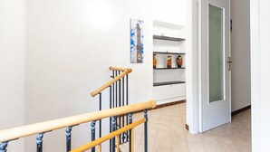 A hallway with a wooden staircase, a door with frosted glass, and a wall-mounted shelf with decorative items. - Ca da Lalla by Wonderful Italy (Varazze)