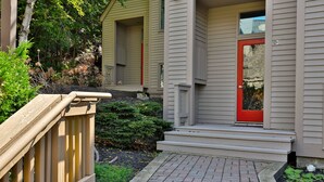 Una casa con una porta rossa, un patio in legno e un vialetto in mattoni che conduce all'ingresso.