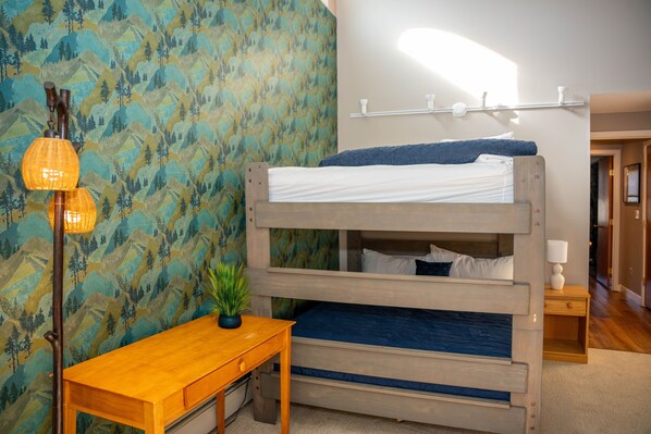 A bunk bed with a wooden frame, a small wooden table, a potted plant, and a wall with a mountain pattern. - Fall Line Condo D4 2 Bedroom Condo (Killington)