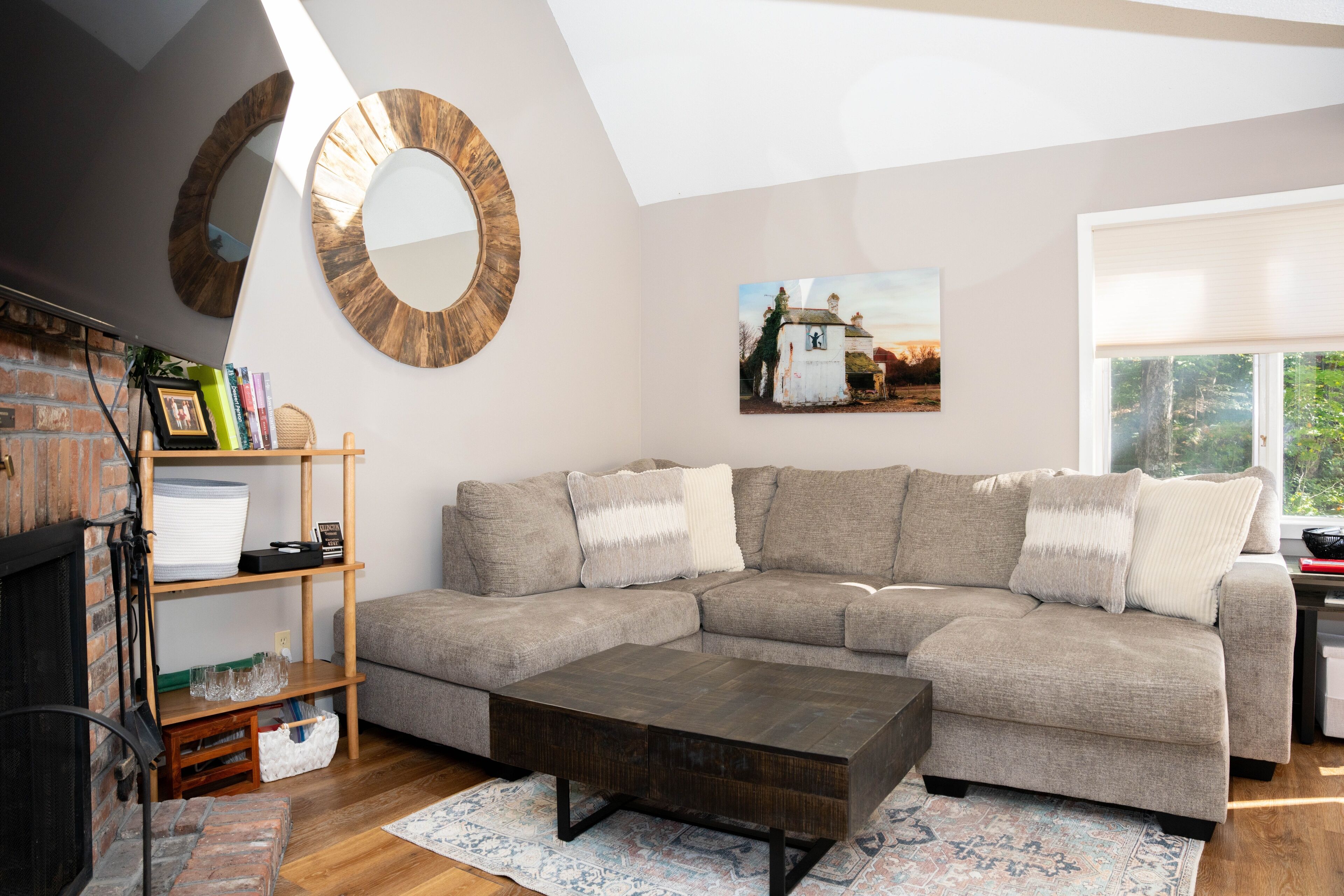 A living room with a sectional sofa, a coffee table, a fireplace, a bookshelf, and a painting on the wall.