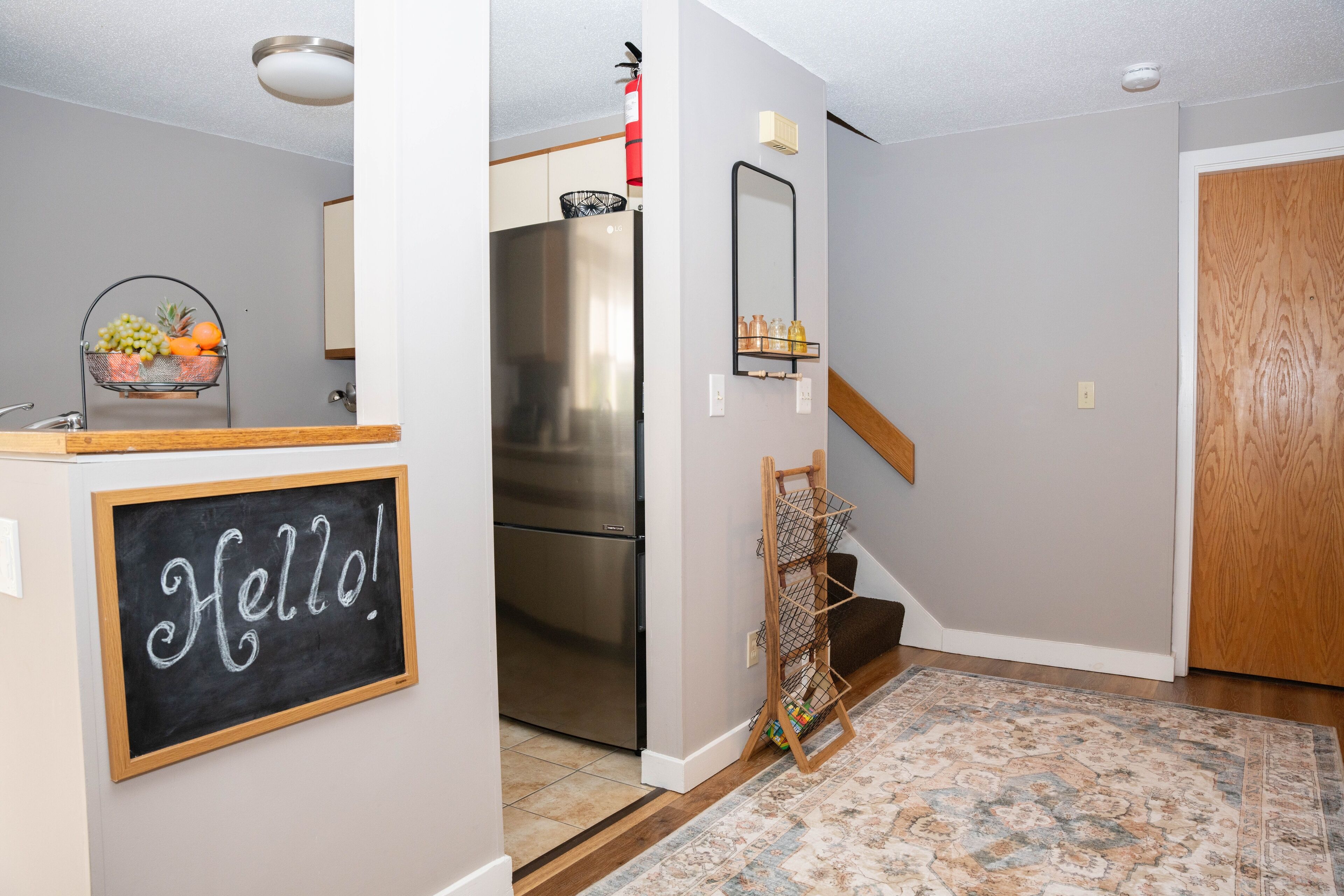 A modern kitchen with a stainless steel refrigerator, a fruit basket, and a 'Hello!' sign on the wall.
