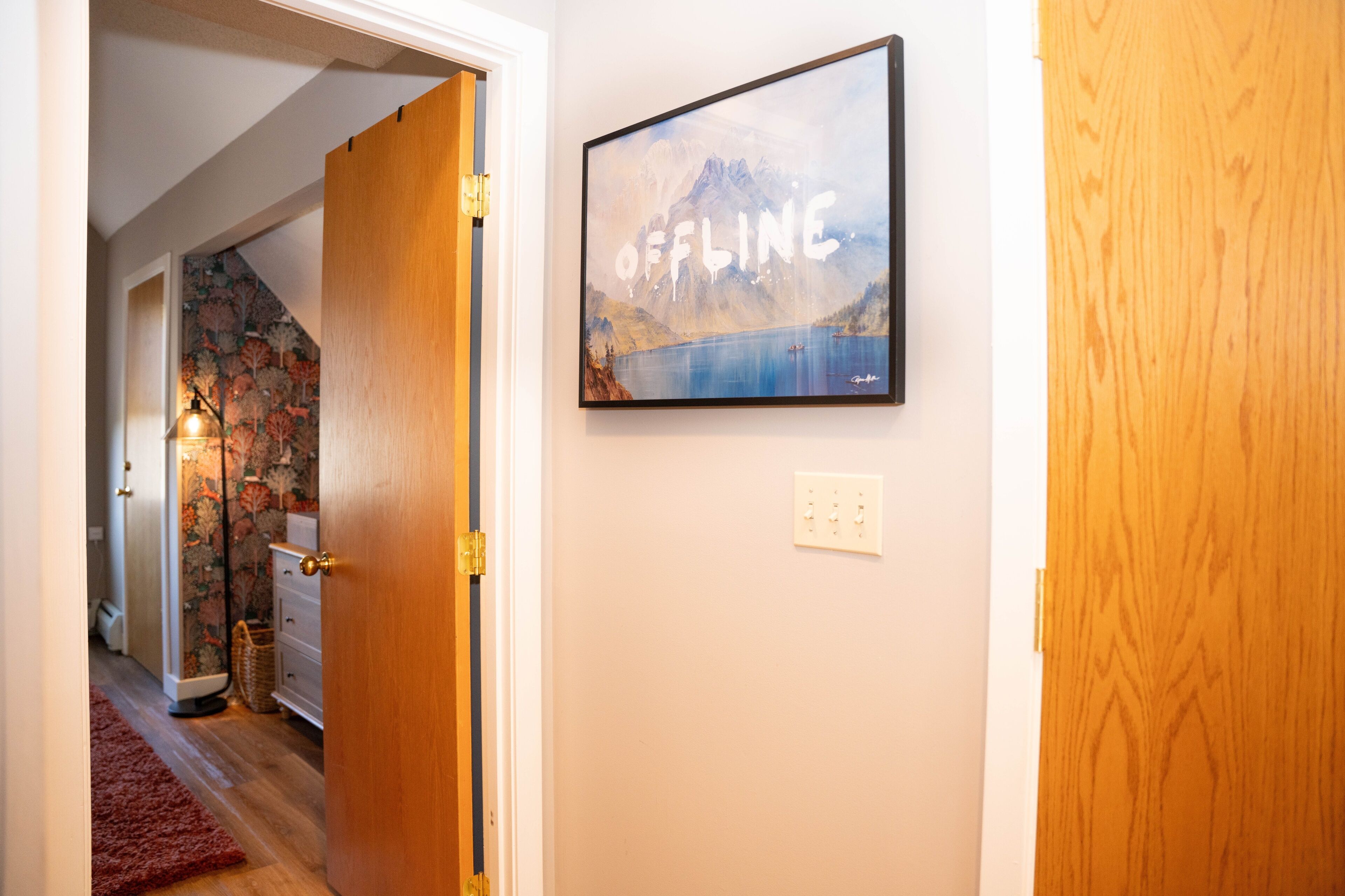 A hallway with a wooden door, a framed picture on the wall, and a patterned carpet.