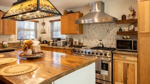 Cucina con mobili in legno, cappa aspirante in acciaio inossidabile, forno a microonde e un'isola grande con lampadario in vetro colorato.