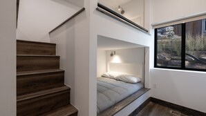 A staircase leading to a loft bedroom with a bed, a window with a view of rocks and grass, and a built-in bench. - Scenic Perch 2 Bedroom Home (Tabernash)