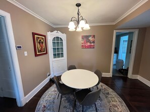 A dining area with a round table, six chairs, a chandelier, a patterned rug, a white door with glass panels, and two framed pictures on the walls. - Entire home, charming 3-2 near the Marietta square! (Marietta)
