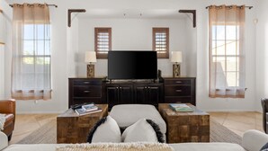 A bedroom with a large bed, a TV, wooden cabinets, and two windows with curtains. - 4BR Heated Pool Estrella Mountain House (Goodyear)