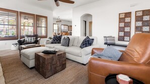 A spacious living room with a white sofa, a brown leather armchair, and a wooden coffee table. - 4BR Heated Pool Estrella Mountain House (Goodyear)