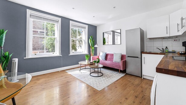 A modern kitchen with white cabinets, a pink sofa, and a large window. - Chic One Bed City Flat (London)