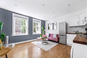 A modern kitchen with white cabinets, a pink sofa, and a large window. - Chic One Bed City Flat (London)