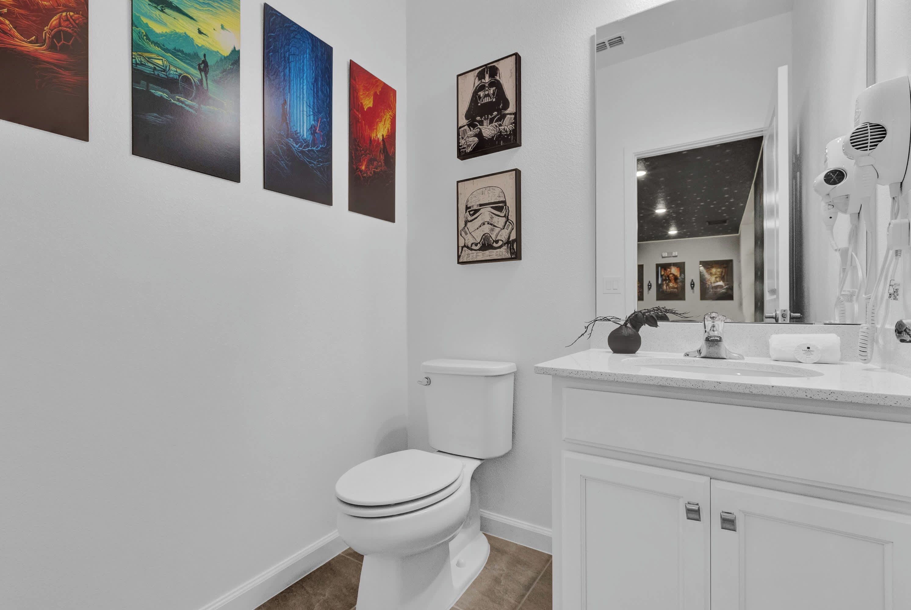 A bathroom with a white toilet, a sink with a mirror, and four framed pictures on the wall.