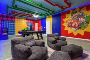 Une pièce aux couleurs vives, avec une table de billard, des fauteuils en forme de sac à haricots et une fresque murale sur le thème de Mario.