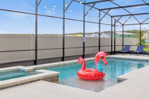 Une piscine avec un flotteur en forme de hippocampe rouge, un espace couvert illuminé de guirlandes lumineuses, et une vue sur les maisons au loin.