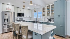 Una cocina moderna con armarios blancos, una isla grande, electrodomésticos de acero inoxidable e iluminación colgante.