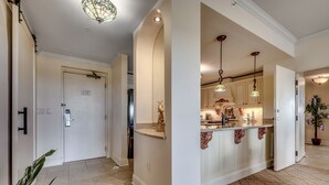 A hallway with a kitchen area, featuring a door, a refrigerator, and a countertop with decorative items.