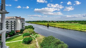 A river with a building on the left, a golf course in the distance, and a clear sky.