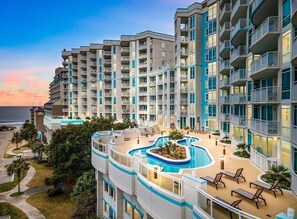 A multi-story hotel with a pool area, balconies, and a view of the ocean.