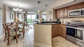 A modern kitchen with wooden cabinets, a large island, stainless steel appliances, and a dining area with chairs and a table. - ⛱️Ocean View Retreat with Private Balcony | Horizon at 77th - Unit 206🌊 (Myrtle Beach)