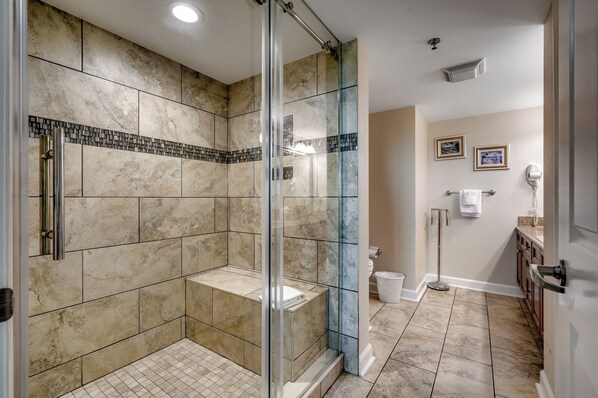 A modern bathroom with a glass-enclosed shower, beige tiles, and a white toilet.
