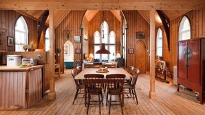A spacious dining area with a long wooden table and chairs, surrounded by wooden walls and large arched windows. - The Tabernacle, Design-led Converted Chapel with Hot Tub, Highland Perthshire (Aberfeldy)