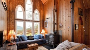 A cozy room with wooden walls, a sofa, a wooden chest, and a stove. - The Tabernacle, Design-led Converted Chapel with Hot Tub, Highland Perthshire (Aberfeldy)