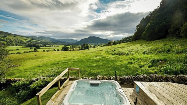 A hot tub in a lush green landscape with mountains in the background. - The Tabernacle, Design-led Converted Chapel with Hot Tub, Highland Perthshire (Aberfeldy)