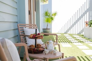 A patio with a table set for tea, including a teapot, cups, and a tray of pastries.
