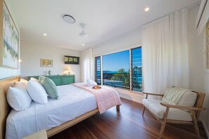 A bedroom with a bed, a chair, a balcony with a view, and a green cabinet. - The Lighthouse (Airlie Beach)