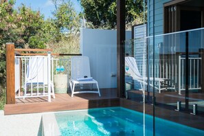 Ein Schwimmbad mit Holzterrasse, weißen Liegestühlen und einem eingezäunten Bereich mit weiteren Sitzmöglichkeiten.