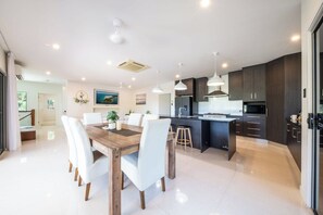 Una cocina moderna con una isla central, iluminación colgante y armarios oscuros.