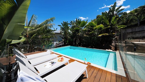 Una piscina con sillas de descanso y plantas tropicales.