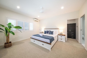 Ein Schlafzimmer mit einem Bett, Nachttischen, einem Schrank und einem Topf mit einer Pflanze.