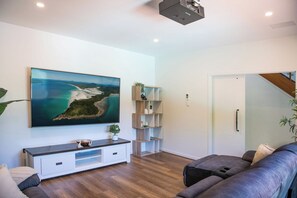 Una sala de estar moderna con un televisor de pantalla plana grande, un mueble de entretenimiento de madera, un sofá gris y una escalera que lleva a un nivel superior.