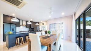 Una cocina moderna con comedor, que incluye una mesa de madera, sillas blancas e iluminación colgante.