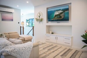 Ein modernes Wohnzimmer mit einer Couch, einem flachbildfernseher an der Wand, einer Wanddekoration und einem großen Fenster.