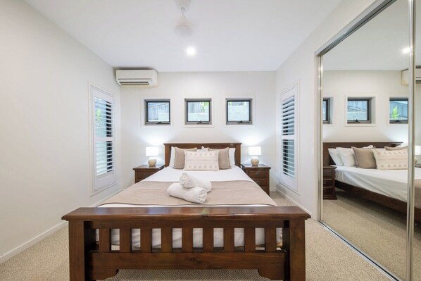 Un dormitorio con cama de madera, mesitas de noche, un espejo y un ventilador de techo.