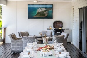 Ein Essbereich mit Tisch, gedeckt für eine Mahlzeit, einem Gemälde einer Küstenlandschaft und Gartenmöbeln.