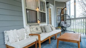 Eine gemütliche Veranda mit einer hölzernen Bank, einer gepolsterten Couch und einem Hängekorbsessel.