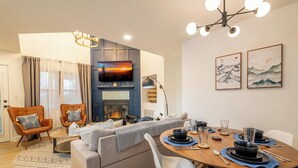 Ein modernes Wohnzimmer mit Kamin, bequemen Sitzgelegenheiten und einem Essbereich, der für eine Mahlzeit gedeckt ist.