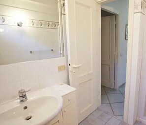 Un baño con lavamanos, espejo y puerta blancos.